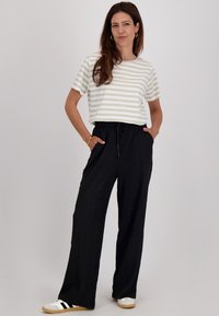 Gestreept shirt met korte mouwen in crème en lichtgroen, gecombineerd met losse zwarte textuurbroek. Sneakers met witte, zwarte en beige accenten.