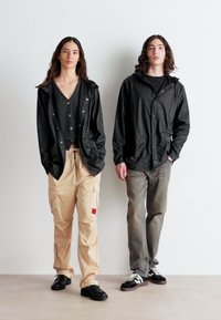 Vestes noires à motifs, pantalons cargo gris et crème, et baskets noires. Les tenues comprennent des boutons, des poches et des textures variées.