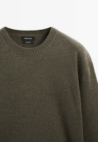 Olivenfarbener Rundhalsausschnitt-Pullover aus feinem Kaschmirstrick mit geripptem Kragen und sichtbarem Markenlabel im Halsbereich.