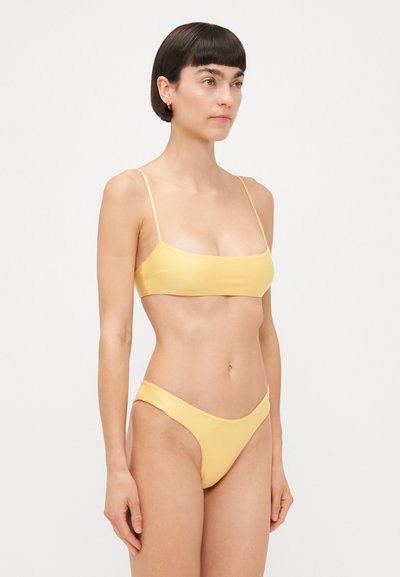 Yellow bikini set featuring thin straps, a bandeau top, and minimalistic high-waisted bottoms. Smooth, matte texture with seamless design.