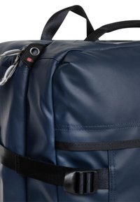 Le sac à dos bleu marine est doté d'un tissu texturé durable, d'une sangle en sangle avec fermeture à boucle, et d'une poche zippée sur le côté.
