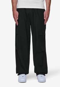 Svart cargobyxor med flera sidofickor, avslappnad passform, i bomullsmaterial och elastiska muddar. Matchas med vita sneakers.