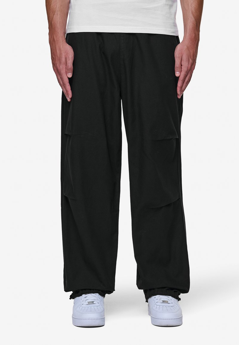 Svart cargobyxor med flera sidofickor, avslappnad passform, i bomullsmaterial och elastiska muddar. Matchas med vita sneakers.