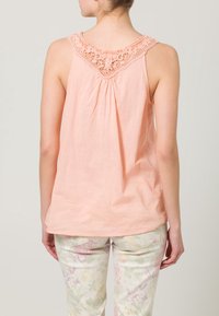 Peach sleeveless top with lace trim at the neckline, gathered back, soft cotton fabric, and a relaxed fit, paired with floral-print pants.