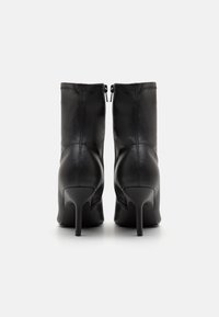 Botines de cuero negro con un diseño elegante, puntas afiladas y tacones altos finos. Incluyen un cierre de cremallera y costuras contrastantes.