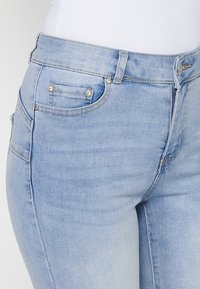 Light blue denim jeans with a fitted design, featuring front and back pockets, silver button accents, and a slightly faded texture.