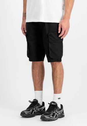 Male wearing black cargo shorts, white crew socks, and black athletic shoes, standing on a white background.