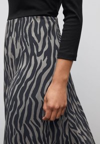 Schwarzes Langarmoberteil, kombiniert mit einem knielangen Rock mit einem grau-dunkelblauen Zebramuster, das einen glänzenden Stoff und einen fließenden Schnitt zeigt.