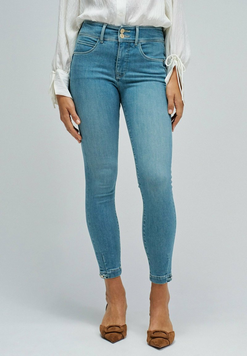 Light blue skinny jeans with a high waist, featuring front pockets and a button closure. The fabric has a smooth texture and slight stretch.
