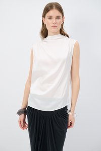 Ärmelloses, cremefarbenes Oberteil mit hohem Kragen, aus glattem Material; kombiniert mit einem schwarzen, drapierten Rock und einem klaren Harzarmband.