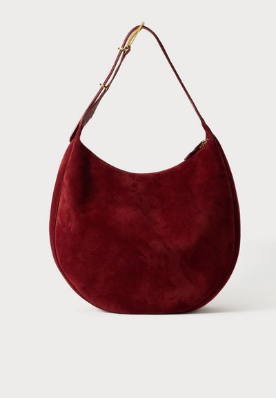 Sac hobo en suède rouge avec une forme arrondie, une texture douce et une large bandoulière dotée de quincaillerie dorée et d'une poche zippée.