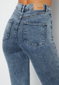 Höga blå denimjeans med en bleknad tvätt, klassisk femfickdesign och en läderlogg på baksidan av midjan.