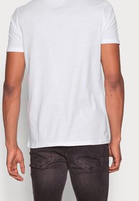 Bílá bavlněná tričko s krátkým rukávem, kulatým výstřihem, hladkou texturou a rovný střih. Nosené s tmavě šedými přiléhavými džíny.