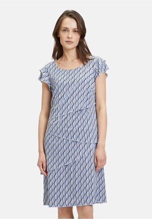 Blau gemustertes Kleid mit gestuften Rüschen, das wellenförmige Linien in Creme und dunklerem Blau zeigt. Kurze Ärmel und knielanges Design.