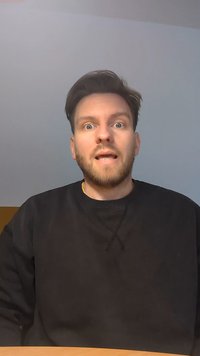 Artimas asmens su trumpais rudais plaukais ir barzda kadras, vilkintis juodą džinsinį švarką. Fonas yra šviesiai mėlynas su geltonu juostu apačioje.