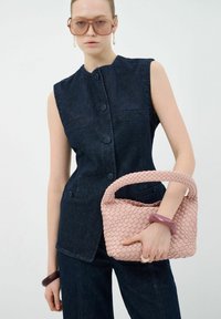 Denim mouwloos top met hoge kraag en knopen aan de voorkant, gecombineerd met een gestructureerde, roze geweven handtas en donkere denim broek.