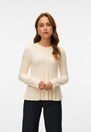Pull crème à côtes avec des manches longues et un ourlet évasé. Il présente un col rond et une texture lisse. Associé à un jean foncé.