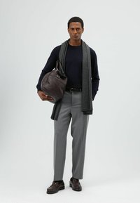 Donkerblauwe trui, grijze sjaal, grijze broek en bruine leren schoenen. Draagt een donkerbruine leren tas met een gladde textuur en een afgeronde vorm.