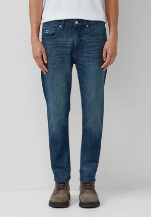 Dark blue denim jeans with a straight cut, featuring whisker patterns, five-pocket design, and a metal button closure. Worn with brown boots.
