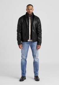 Schwarze Lederjacke mit hohem Kragen, Reißverschluss und gesteppten Akzenten, kombiniert mit hellblauen Jeans und schwarzen Stiefeln. Glatte Textur.