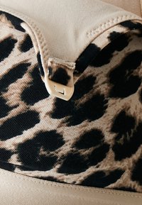 Bralette de estampado de leopardo con colores beige y negro, textura de tela suave y cierre de gancho de plástico en la parte delantera.