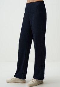 Marineblauwe, gestructureerde wijde pantalon met een geometrisch patroon, voorzien van een elastische tailleband en zachte stof, gecombineerd met lichtgekleurde sneakers.
