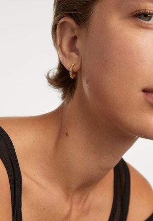 Orecchino a cerchio in oro con accenti di pietre trasparenti. Forma rotonda e finitura lucida; mostrato in un primo piano sull'orecchio di un modello.
