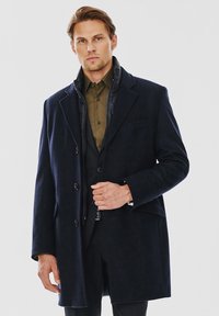 Granatowy płaszcz wełniany z mieszanką, z kołnierzem z wycięciem, zapięciem na guziki i pikowaną podszewką, z przednią kieszenią i dopasowanym krojem.