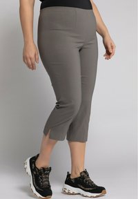 Pantalons grisons cropped avec un design ajusté, présentant des fentes sur le bord. Assortis à des baskets noires et beiges avec un tissu texturé.