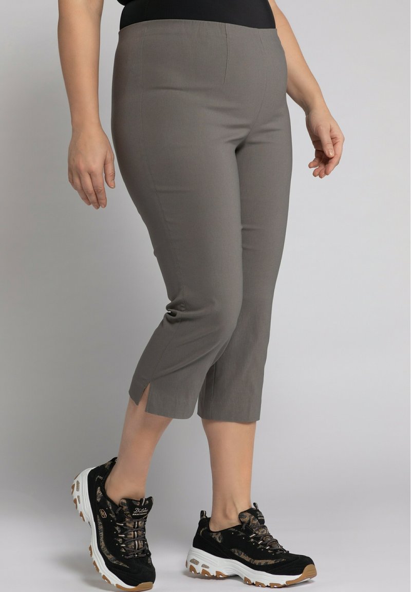 Pantalons grisons cropped avec un design ajusté, présentant des fentes sur le bord. Assortis à des baskets noires et beiges avec un tissu texturé.