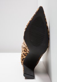 Chaussure à talon haut imprimé léopard avec bout pointu, semelle inclinée montrant le dessous texturé noir sur fond blanc.