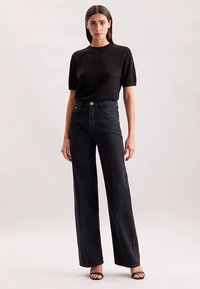 Czarny top z krótkim rękawem w połączeniu z czarnymi, szerokimi spodniami z wysokim stanem. Gładka tkanina o klasycznej teksturze denimu. Minimalistyczny design bez widocznych wzorów.