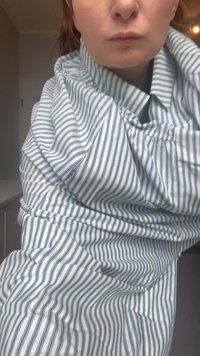 Camicia di stoffa a righe blu e bianche con colletto, texture arricciata e vestibilità ampia, che pende sul braccio della persona.
