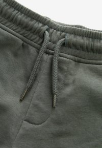Des sweatpants vert foncé en mélange de coton doux, avec une taille élastique et un cordon de serrage, ainsi qu'une poche latérale. Texture lisse avec des détails cousus.