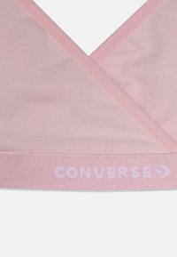 Lyserød BH med en omslagdesign; blødt stof og elastisk bånd med teksten "CONVERSE". Glat tekstur og minimale syninger.