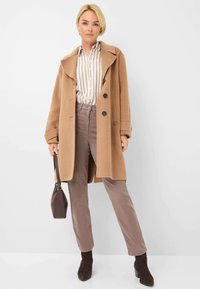 Lichtbruin wollen jas met grote kraag en zwarte knopen, gecombineerd met een beige gestreept overhemd, taupe broek en bruin suède enkellaarsjes.