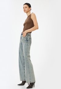 Brun ribbad ärmlös topp tillsammans med ljusblå överdimensionerade jeans och svarta spetsiga klackar. Figurerna är smala med en slät textur.