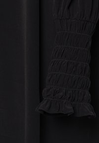 Tejido de vestido negro con una textura suave; presenta un detalle de manga agrupada y con volantes y un cuerpo ajustado, enfatizando una silueta elegante.
