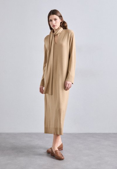 Strikket tan kjole med nøglehul-udskæring og lange ærmer, parret med et matchende tørklæde og brune loafers. Glat tekstur, ankel-længde design.