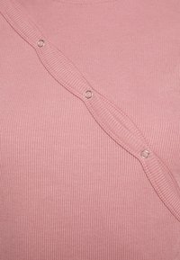 Rosa ribbad top med rund halsringning, som har en diagonalt placerad knappslå med runda metallknappar längs ena sidan.