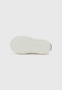 Suela de zapato de goma blanca con superficie texturizada y patrones elevados, forma redondeada y pequeño acento de marca cerca del talón.