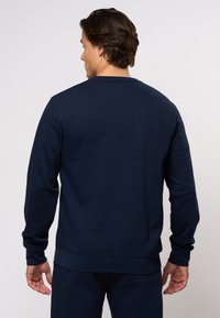 Námornícky modrý pulóver zo soft cotton zmesi. Má okrúhly výstrih, dlhé rukávy a rebrované manžety a lem. Minimalistický dizajn.