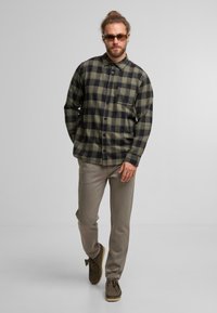 Groene en zwarte geruite overhemden met een borstzak; gecombineerd met lichtgrijze broeken en bruine schoenen.