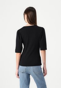Sort tætsiddende top med korte puffærmer, rund hals, lavet af glat stof. Kombineret med lyseblå jeans, som viser en afslappet pasform.