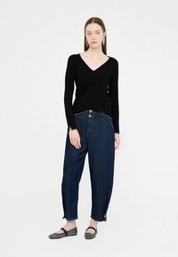 Juodas V formos kaklo megztinis su ilgomis rankovėmis, derinamas su laisvo kirpimo tamsiai mėlynais džinsais, turinčiais sagų užsegimą ir susuktais rankogaliais. Pilki lygūs batai.