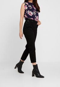 Hedvábná blůza s květinovým potiskem v námořnické modři, zdobená volánovým výstřihem, v kombinaci s černými džíny s vysokým pasem a černými kotníkovými botami na blokovém podpatku.