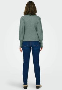 Grön rullad tröja med puffärmar, figurnära design, kombinerad med blå slim fit-jeans. Tröjan har en hög krage och strukturerad tyg.