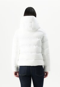 Witte pufferjas met een hoge kraag en elastische manchetten. Heeft een gewatteerd ontwerp en een getailleerde silhouet. Draagt over donkere denim.