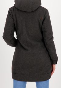 Ciemnoszary wełniany płaszcz z kapturem, o nieco dłuższym kroju, minimalistycznym designie i małym brązowym logo na plecach.