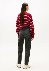 Röd och rosa randig stickad tröja, avslappnad passform, kombinerad med högmidjade svarta jeans och vita sneakers, sedd bakifrån.